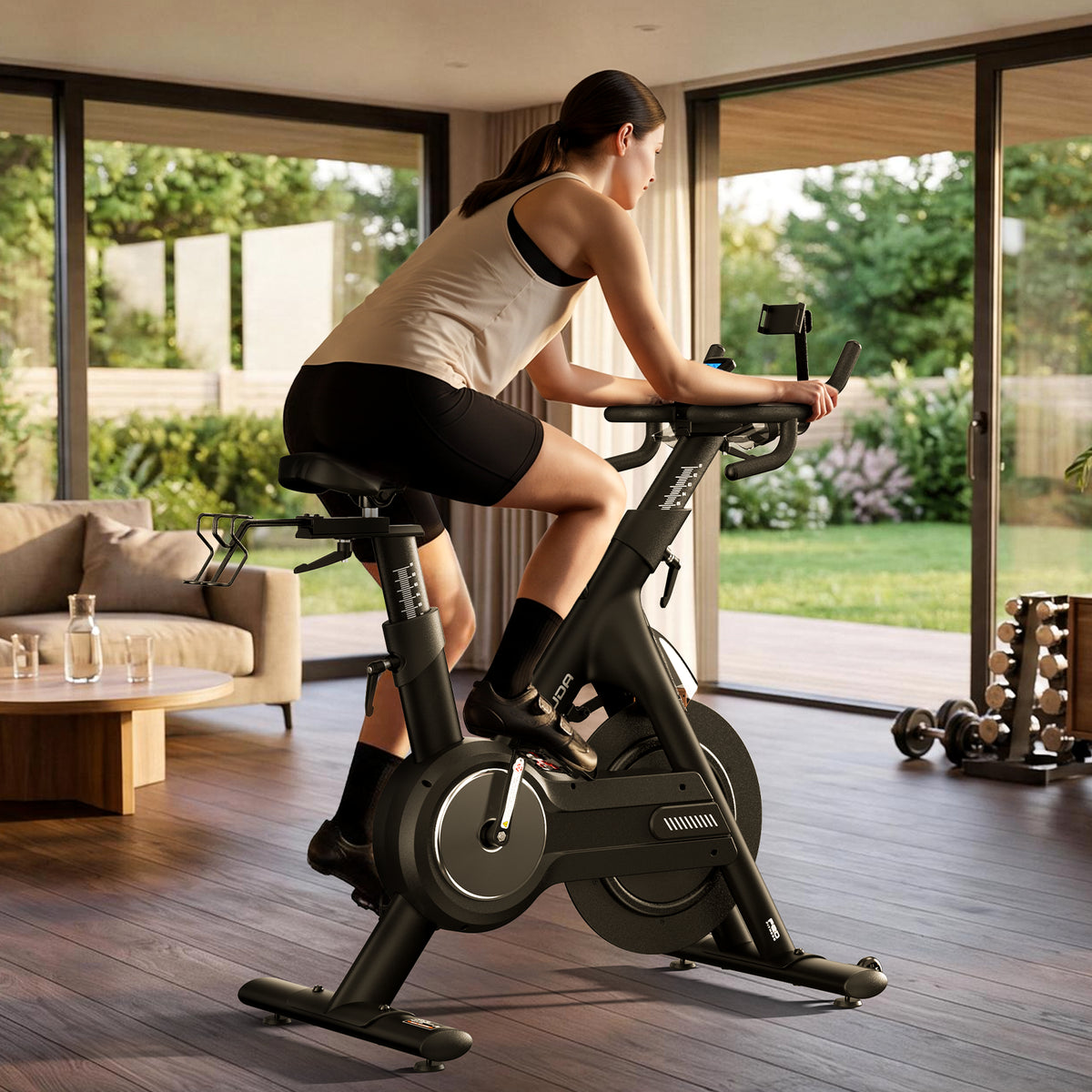 A woman riding the FED Fitness Yosuda EB3C indoor exercise bike in a modern home gym with large windows, wood floors, and a sofa in the background.