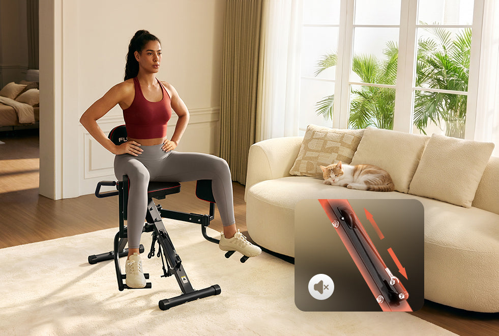 A woman sits on a compact leg extension exercise machine in a bright living room, with a beige sofa, window, and a cat resting on the couch in the background. An inset graphic in the lower right shows a close-up of the machine's leg assembly.