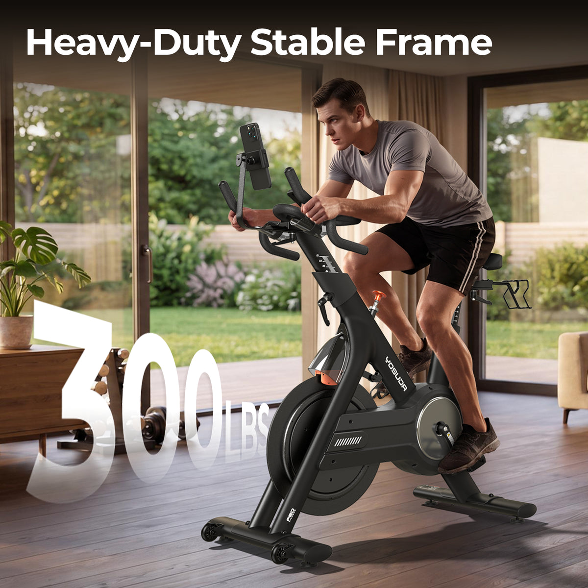 A man rides the FED Fitness Yosuda series EB3C indoor exercise bike in a modern living room with large windows and outdoor greenery visible. The heavy-duty stable frame can support up to 300 lbs.
