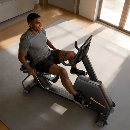 Man exercising on a recumbent bike in a bright room with large windows.