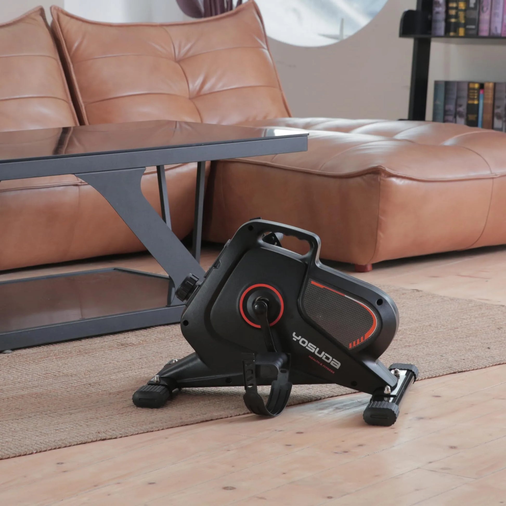 Black exercise bike with red accents on a wooden floor in a living room setting.